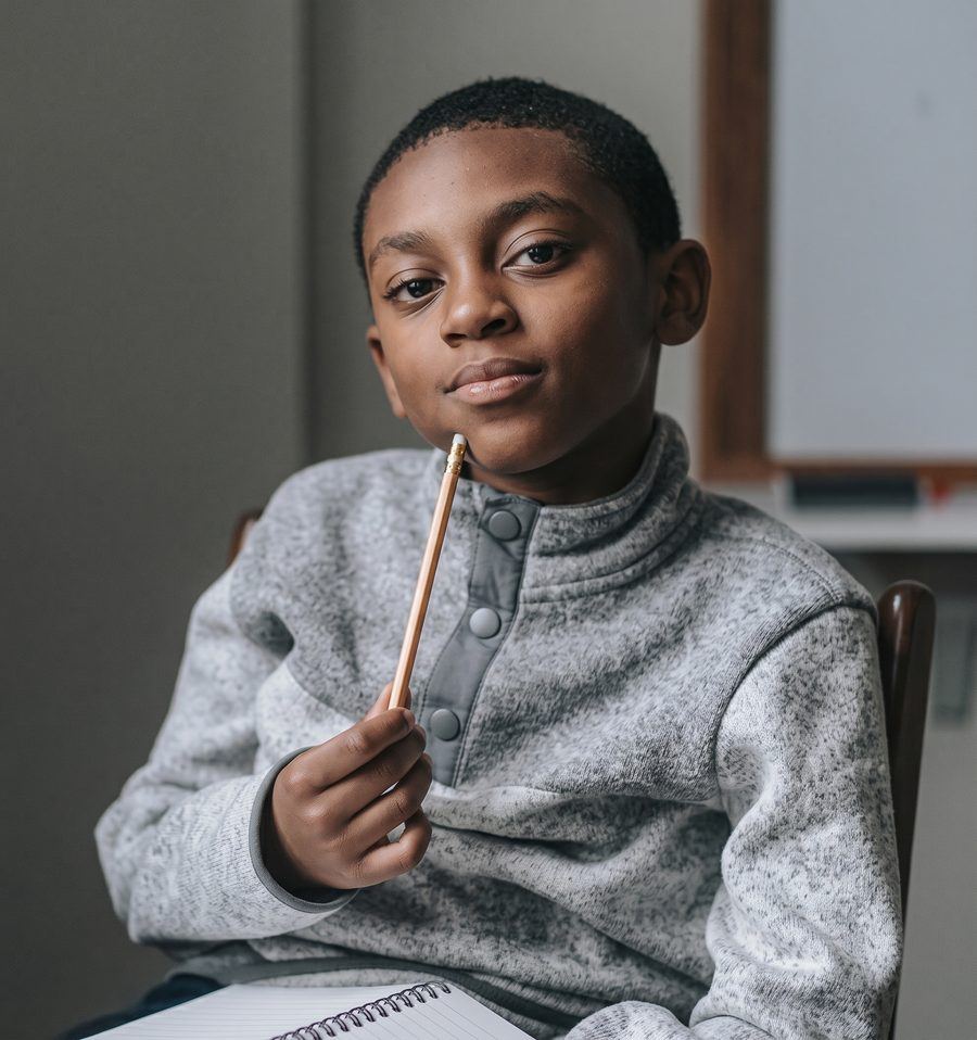 A young Black boy at a desk holding a pencil to his chin, representing academic success coaching in Chicago