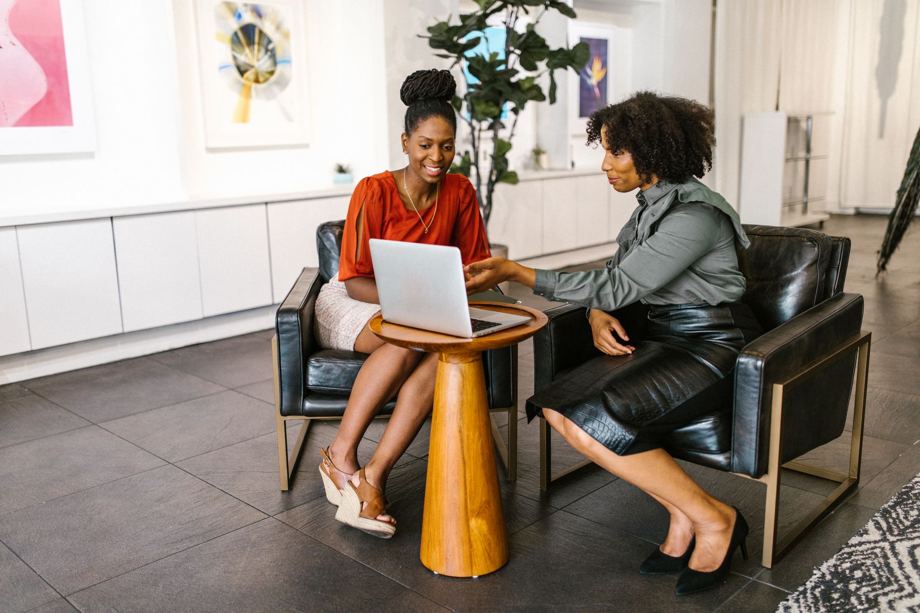 Two Black women in a career coaching conversation, reviewing a laptop together at a table in a bright office