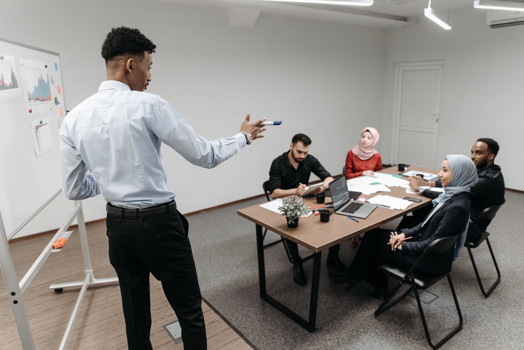 A Black professional leading an organizational strategy session at a whiteboard while a diverse team takes notes around a conference table