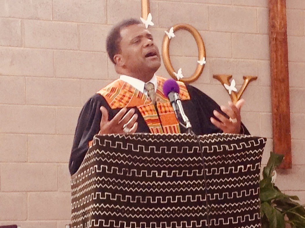 Dr. Kahan Sablo preaching in a black robe and kente stole at a pulpit