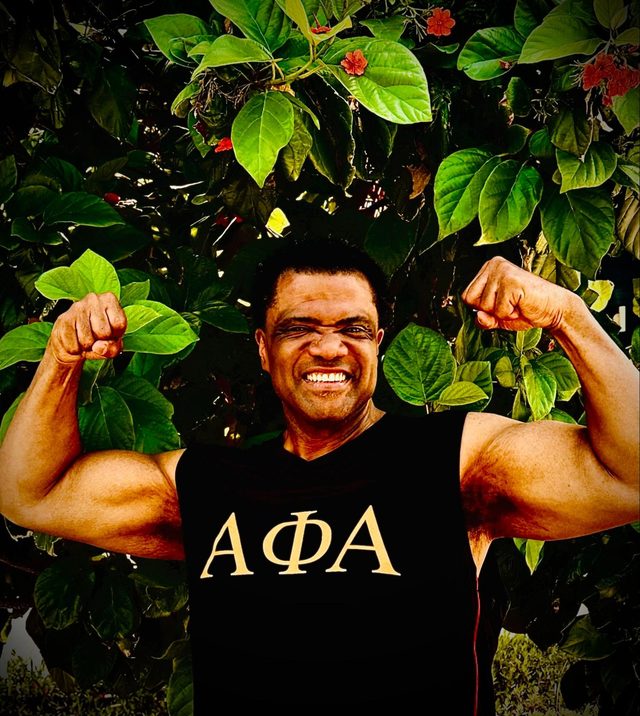 Dr. Kahan Sablo smiling and flexing both arms in a black tank top outdoors