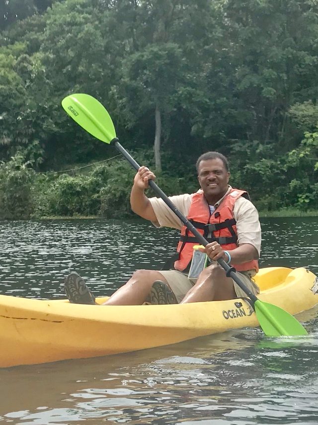 Dr. Kahan Sablo smiling in an orange life vest paddling a yellow kayak